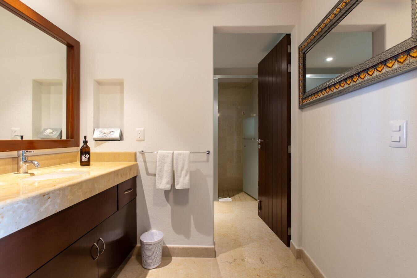 A bathroom with a marble sink, a large mirror, a bottle of soap, and a towel rack.