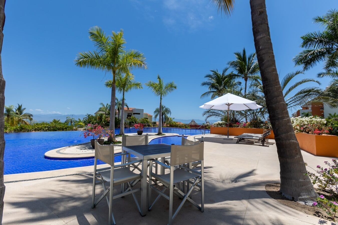 Un espace aménagé au bord de la piscine, avec une table et des chaises, des palmiers et une vue sur l’océan.