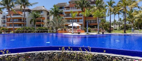 Un resort con una gran piscina rodeada de palmeras y un edificio con varios balcones.