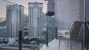 Un balcon donnant sur des immeubles de grande hauteur, une petite table et deux chaises.