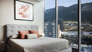 Une chambre dotée d’un grand lit, offrant une vue sur la ville, et ornée d’une œuvre d’art encadrée au mur.