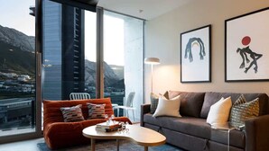 Un salon moderne avec un canapé, une table basse et une vue sur un paysage montagneux grâce à de grandes fenêtres.