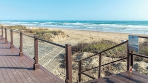 Une promenade en bois mène à une plage où un panneau indique qu’il est interdit de jeter des déchets, notamment du verre, et qu’il est obligatoire de tenir les animaux en laisse.