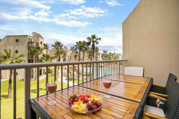 A balcony with a table, two glasses of red beverage, and a fruit bowl.