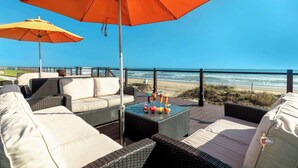 Une terrasse au bord de la plage, avec des meubles en osier, une table où sont disposées des boissons et une vue sur l’océan.