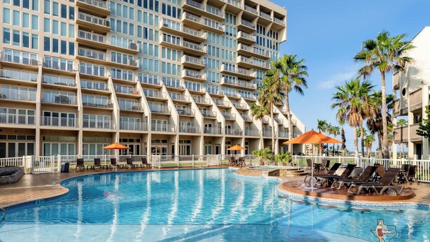 Un hôtel doté d’une grande piscine, de nombreux balcons et de palmiers.