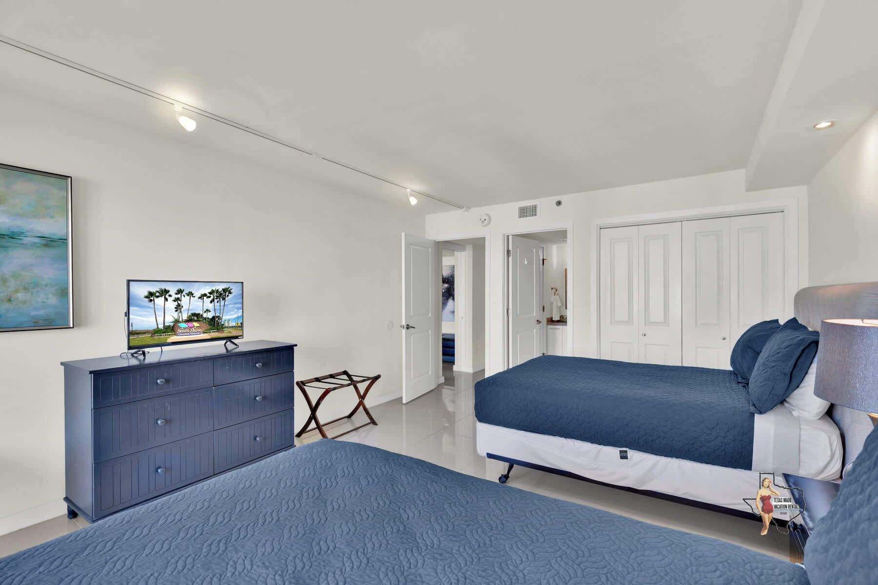 Ein Schlafzimmer mit zwei Betten, einem Schminktisch, einem Fernseher und einem Bild.