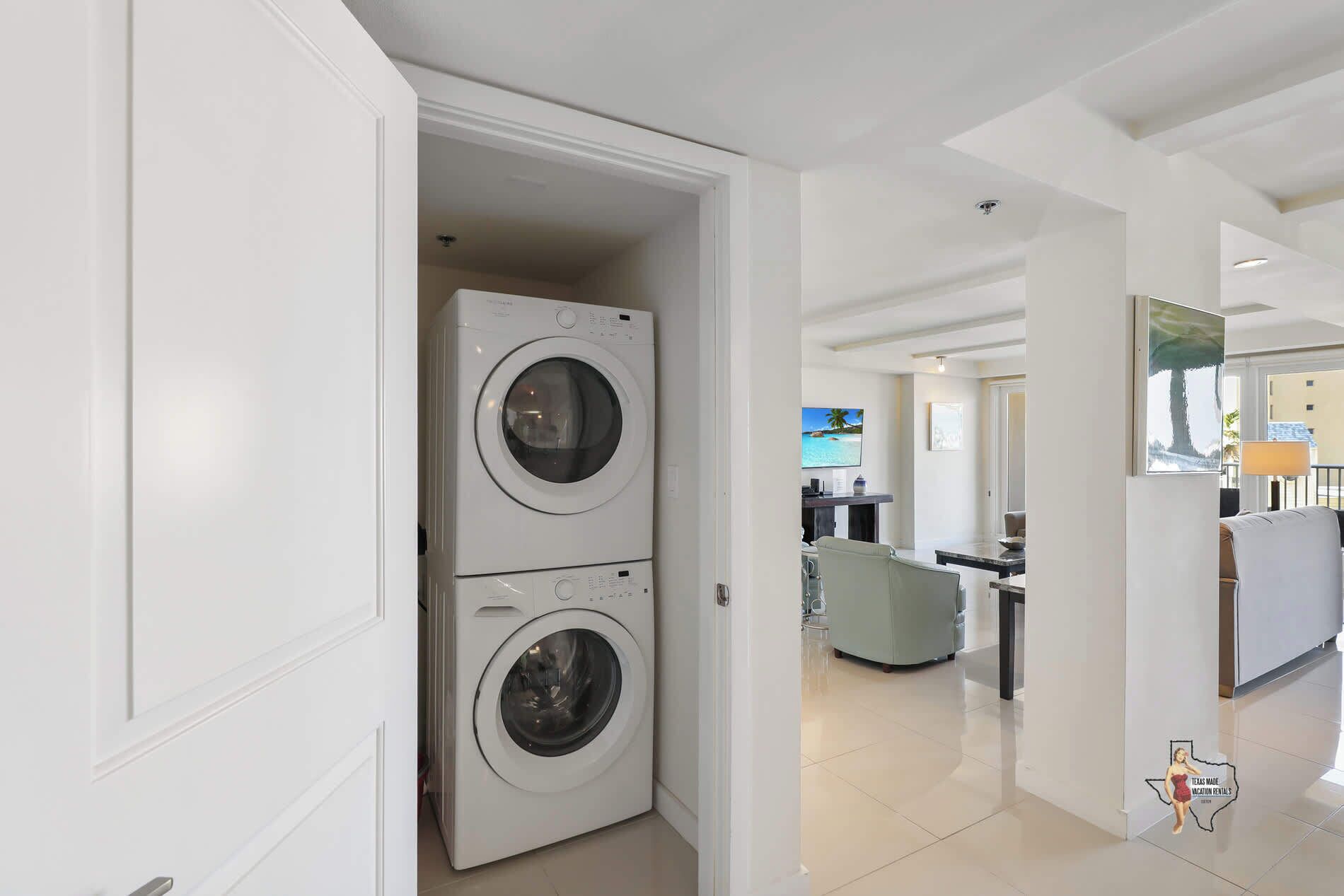 A laundry room with two stacked washing machines, a kitchen area with a dining table and chairs, and a view of the outside through a window.