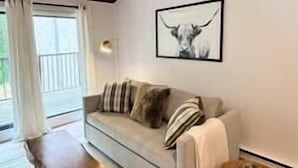 A living room with a sofa, a wooden bench, a round wicker side table, and a framed artwork on the wall.