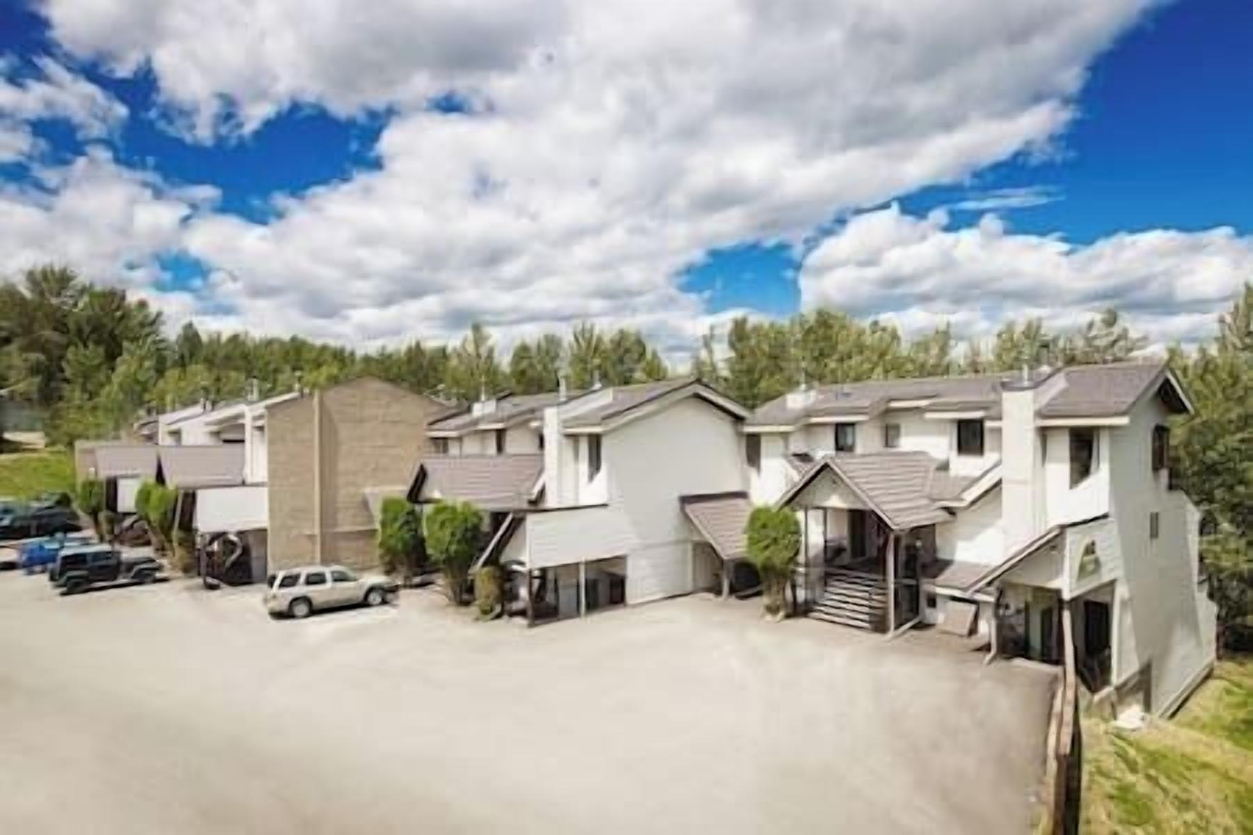 Række moderne parcelhuse med tilhørende garager, en asfalteret indkørsel og et baggrund af træer samt en klar himmel.