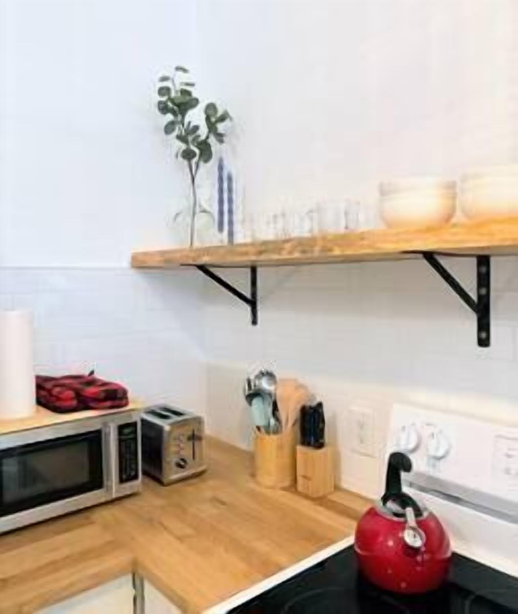 A kitchen with a microwave, toaster, kettle, and a shelf with bowls and utensils.