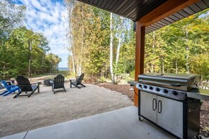 Un patio al aire libre con una parrilla, dos sillas Adirondack y una mesa.