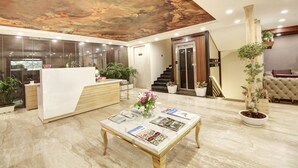 Un hall d’hôtel avec un comptoir d’accueil, une table basse en marbre avec des magazines, des plantes en pot et un escalier menant à un autre étage.