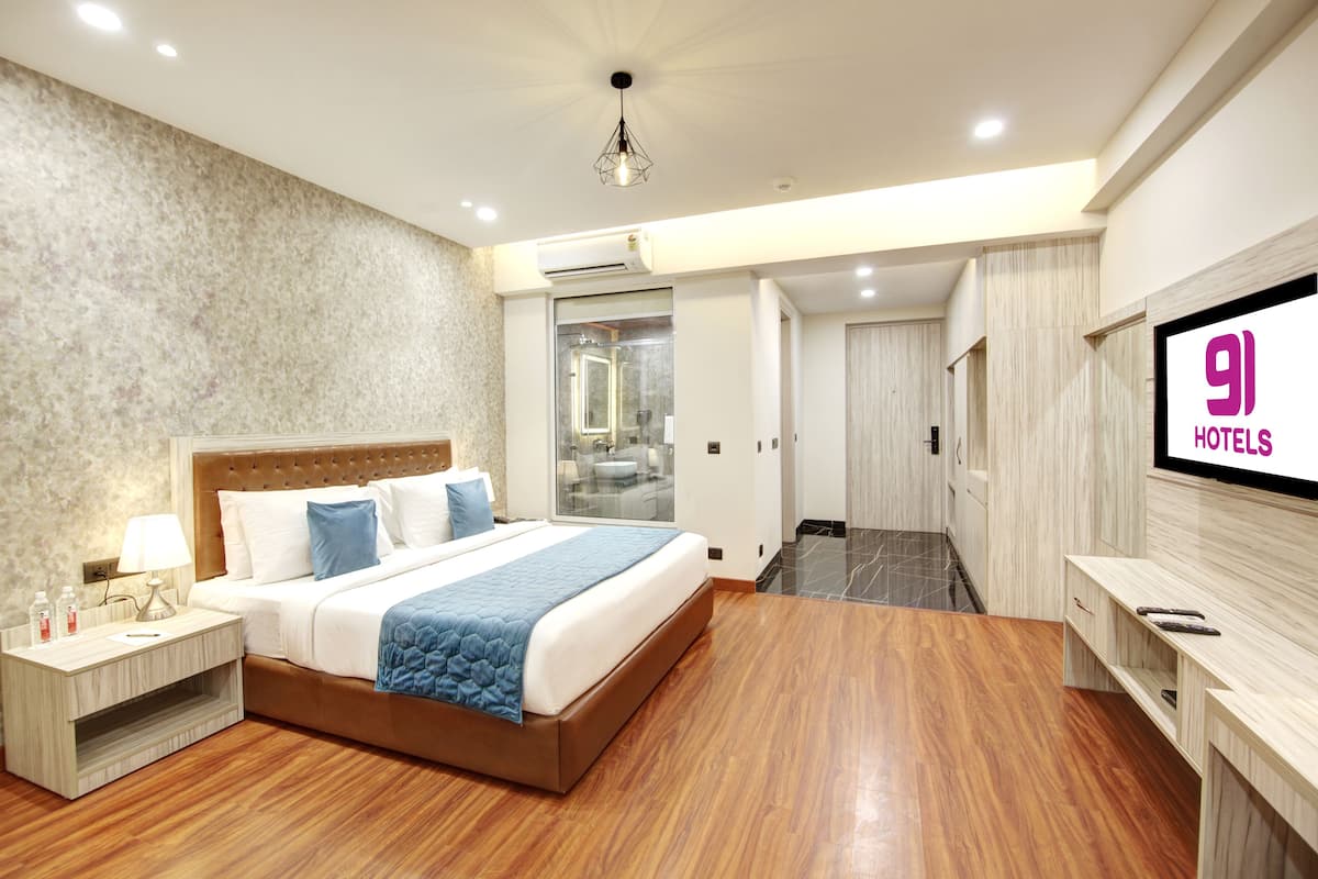 Una camera d'albergo moderna con un letto grande, una TV, un comodino e un bagno visibile tramite una porta in vetro.