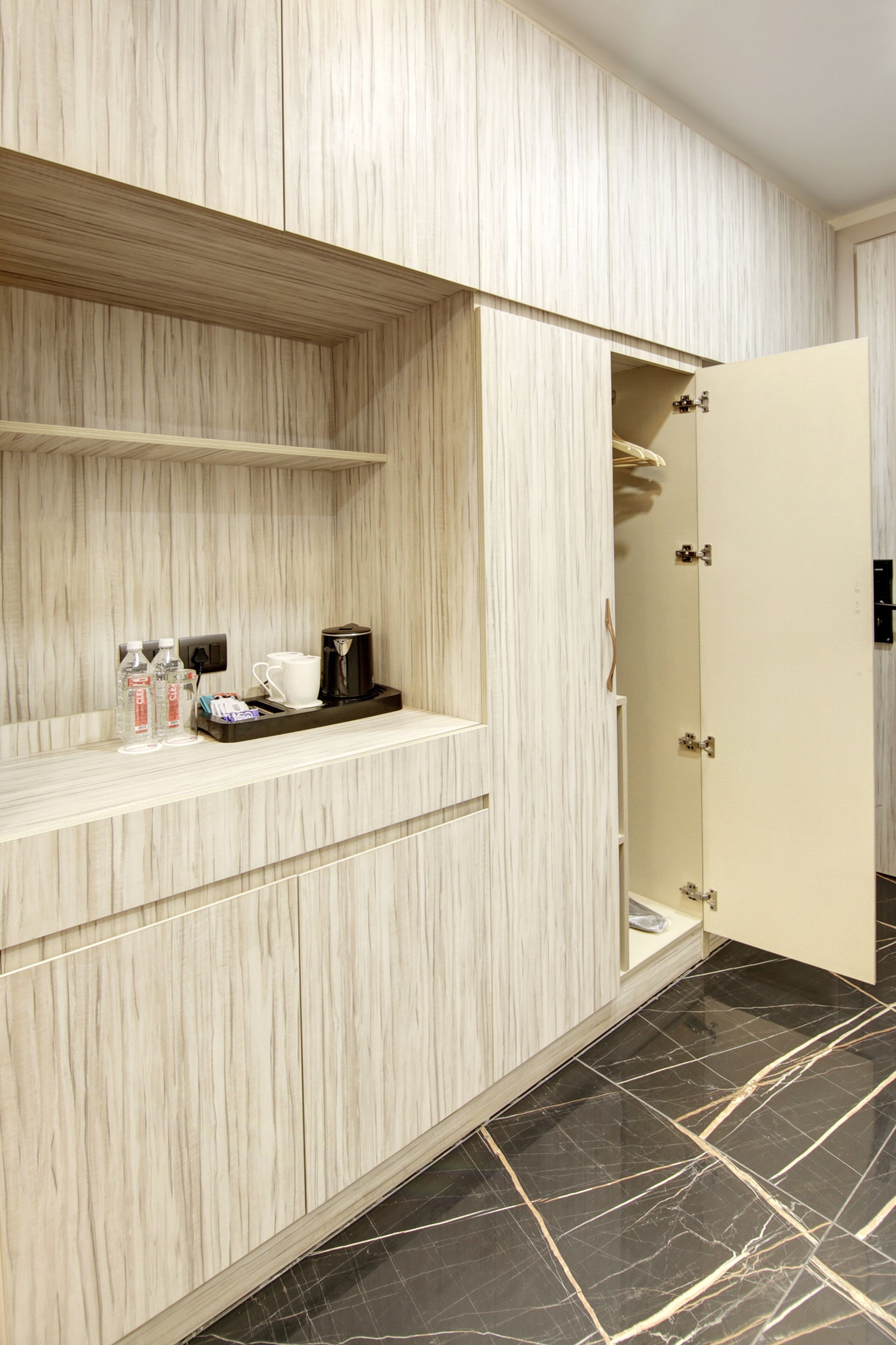 A hotel room with a wooden vanity, a coffee maker, and a tray with bottles and cups.