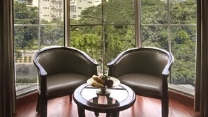 Une pièce d’angle avec deux fauteuils en cuir et une petite table ronde, de grandes fenêtres offrant une vue sur les bâtiments et la verdure.