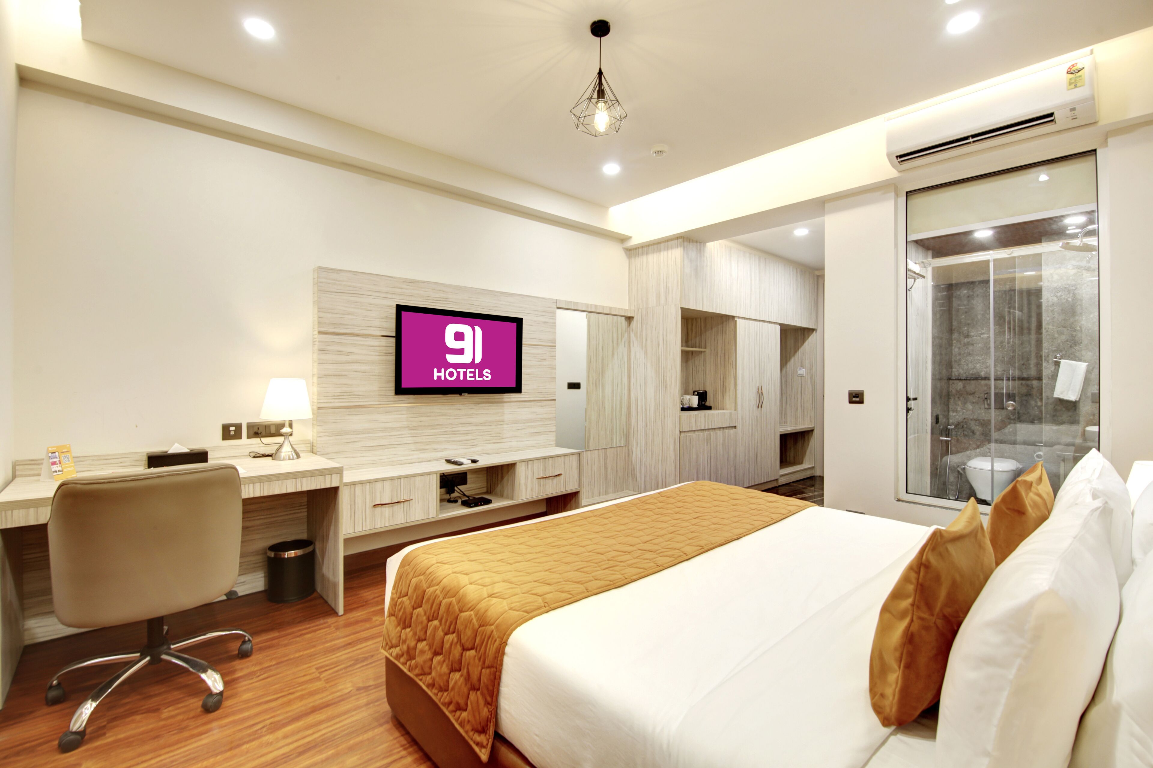 A hotel room with a bed, desk, chair, TV, wardrobe, and a shower area.