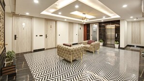 Un hall d’entrée moderne avec un sol à motifs géométriques, des sièges confortables et un luminaire central.