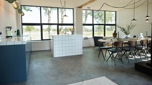 Une cuisine moderne dotée d’un grand îlot central, bénéficiant d’une abondante lumière naturelle grâce à de grandes fenêtres, et comprenant un coin repas avec des chaises et une table.