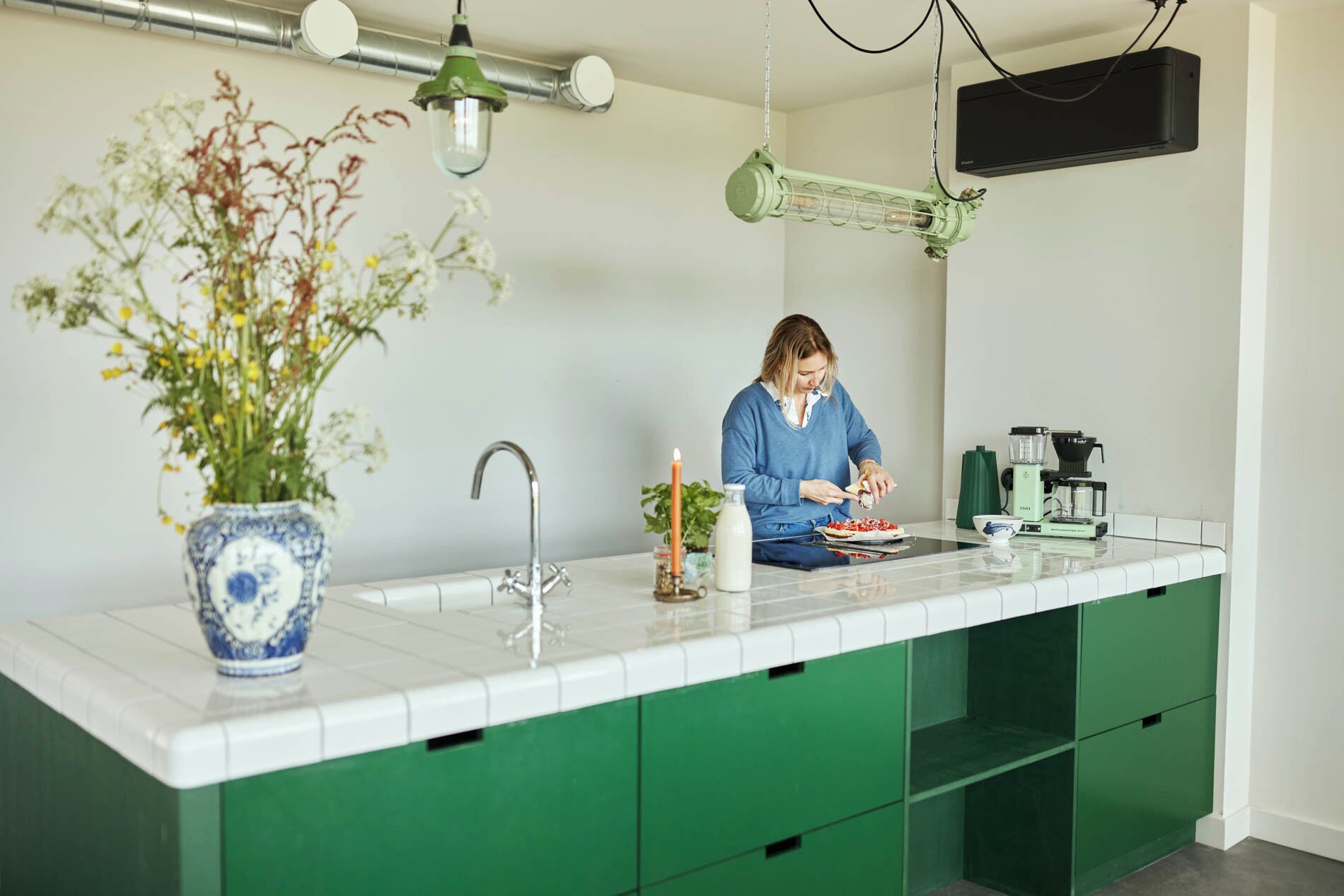 Eine moderne Küche mit einer grünen Arbeitsplatte, einem weißen Spülbecken und einer Person, die gerade Essen zubereitet.