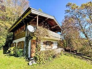 Una cabaña de madera con balcón, rodeada de árboles y un cielo despejado.