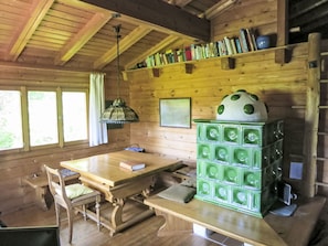 L’intérieur d’un chalet en bois comprend une table à manger, des chaises, un luminaire suspendu, une bibliothèque et un appareil électroménager vert.