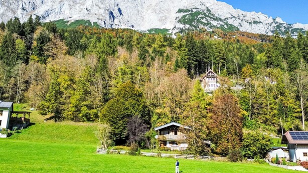 Un paysage de montagne avec une maison entourée d’arbres et un ciel dégagé.