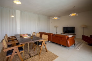 A modern living room with a wooden dining table, leather sofa, and a flat-screen TV.