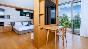A modern bedroom with a large bed, a wooden desk, and a sliding glass door leading to a balcony with a view of greenery. - SeaView 3BR Duplex BluePoint 88 Patong (Patong)