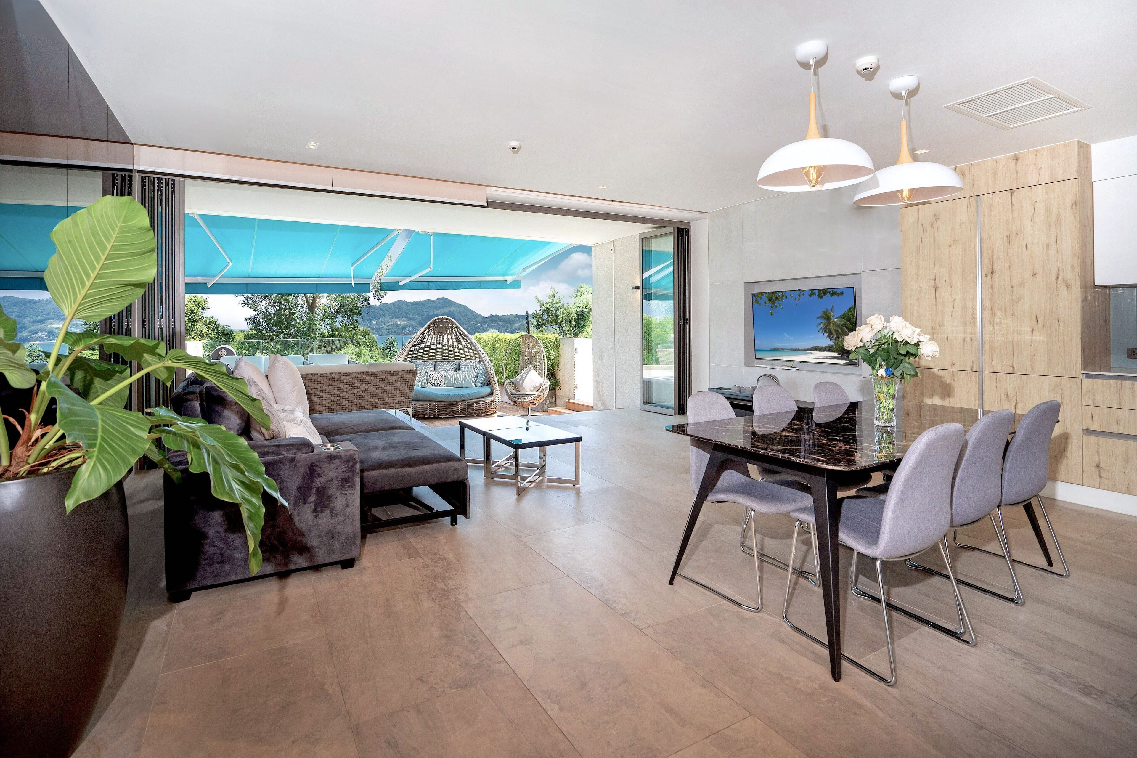 A modern living room with a sofa, chairs, a dining table, and a large window offering a view of the outdoors.