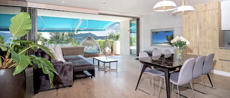 Una sala de estar moderna con un sofá, sillas, una mesa de comedor y un amplio ventanal con vistas al exterior.