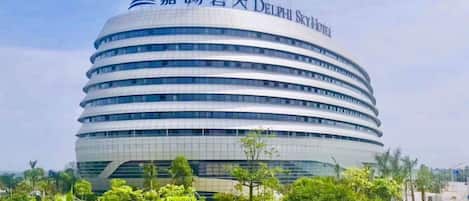 A modern, multi-story hotel with a distinctive curved architecture and a prominent logo at the top.
