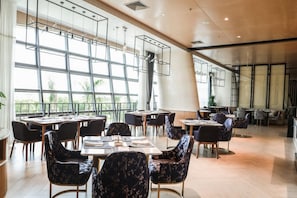 A spacious indoor dining area with multiple tables and chairs, large windows, and a modern ceiling design. - Delphi SKY Airport Hotel (Nanning)