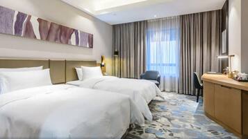 A hotel room with two beds, a desk, a chair, and a large window with curtains.