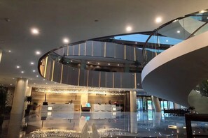 A modern hotel lobby with a central reception desk, a glass elevator, and a spacious atrium. - Delphi SKY Airport Hotel (Nanning)