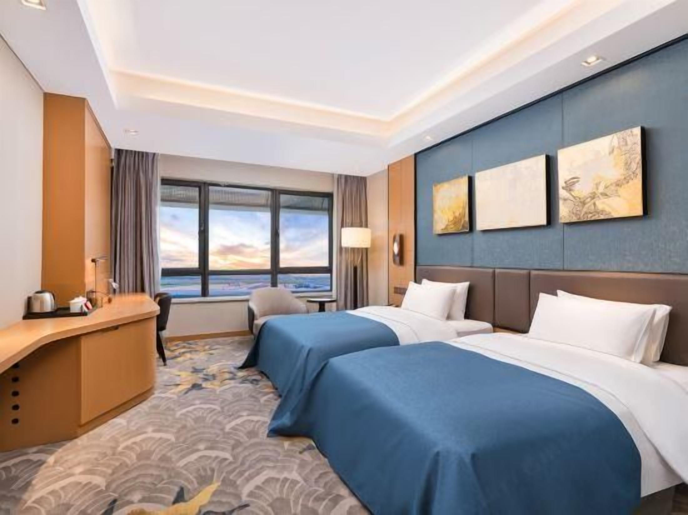 Habitación de hotel con dos camas, un escritorio y vistas a la ciudad.