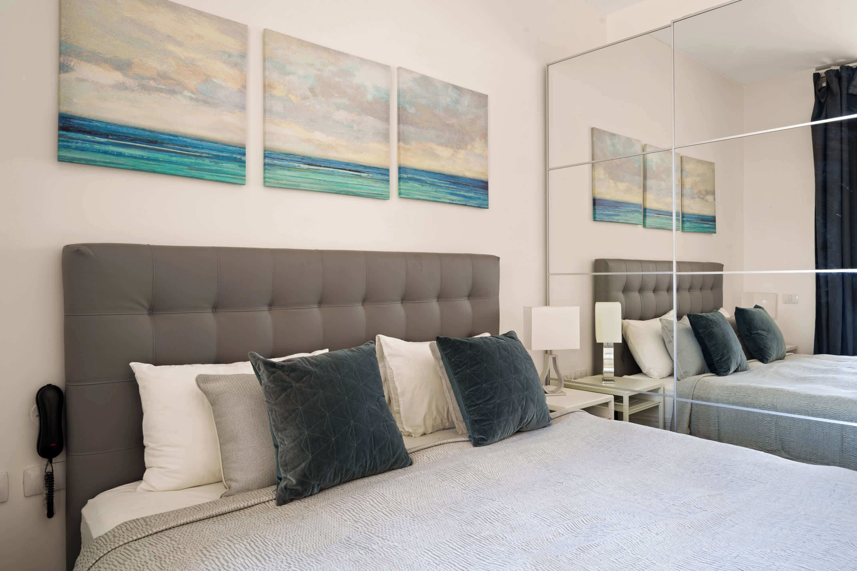 A hotel room with a large bed, a nightstand, a lamp, and artwork on the wall.