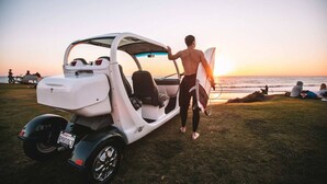 A white golf cart parked on a grassy area with a sunset in the background. - Location Location! Steps to beach, parking (San Diego)