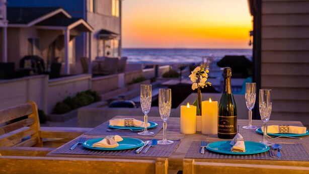A table set for a meal with a bottle of wine, glasses, and candles, overlooking a sunset and ocean view. - Location Location! Steps to beach, parking (San Diego)