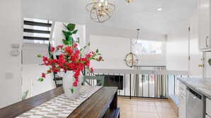 A modern kitchen with white cabinetry, a wooden dining table, and a vase of red flowers. - Location Location! Steps to beach, parking (San Diego)