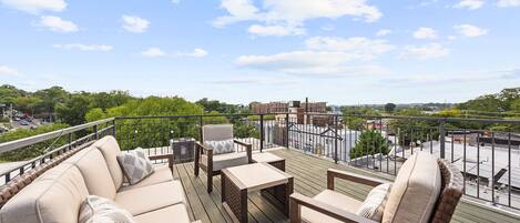 A deck with outdoor furniture, a view of a cityscape, and a clear sky.