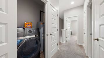 A laundry room with a front-loading washer and dryer, a bottle of detergent, and a water heater.