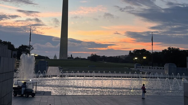 Un grand obélisque, avec une fontaine d’eau au premier plan et un coucher de soleil en arrière-plan.