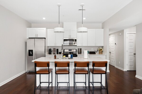 A modern kitchen with white cabinets, a central island with bar stools, stainless steel appliances, and pendant lighting.