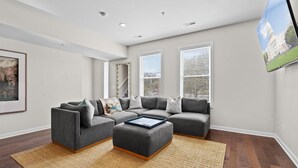 A living room with a sectional sofa, a coffee table, and a large TV mounted on the wall.