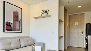 A modern living room with a sofa, a coffee table, a framed cityscape picture, a small shelf with a plant, and a door with a sign.