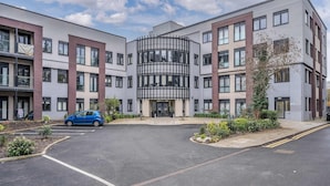 En moderne bygning med flere etager, et centralt atrium, parkeringsplads og beplantede områder.