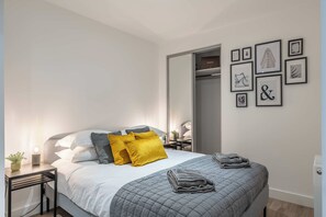 A modern bedroom with a bed, bedside tables, a nightstand, a lamp, a potted plant, and a closet.
