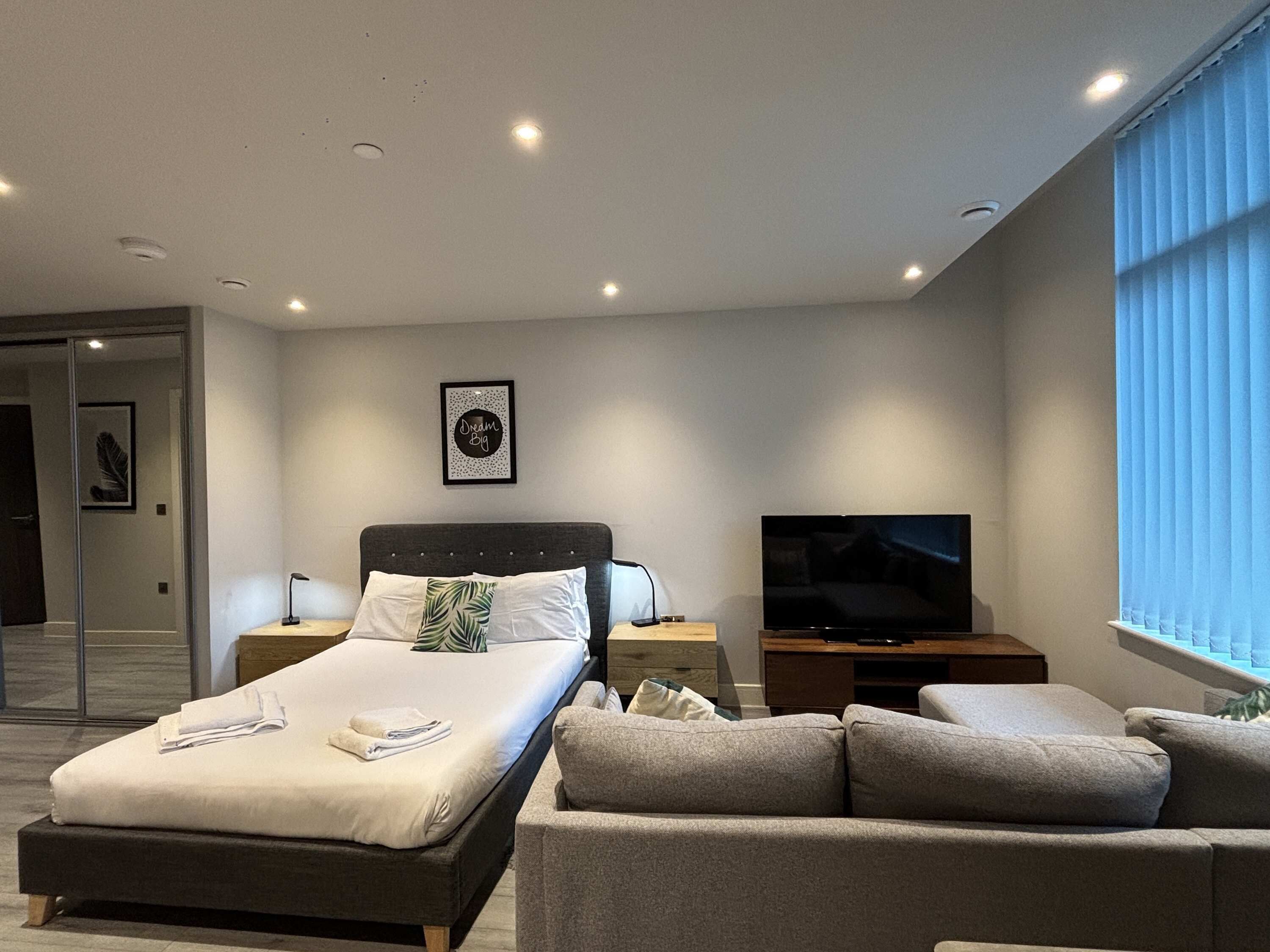 Een moderne slaapkamer met een bed, een televisie, een bank en een ingelijst schilderij aan de muur.