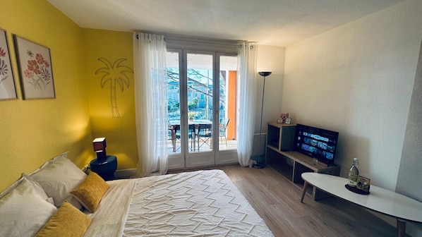 A hotel room with a bed, a TV, a desk, and a balcony with a view of buildings. - Lemon house rental with marina view close to the sea and shops  (Cogolin)